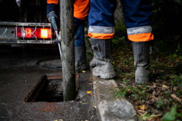 Drain cleaning service in Fulham, technician using equipment near a drain, wearing safety gear and boots.