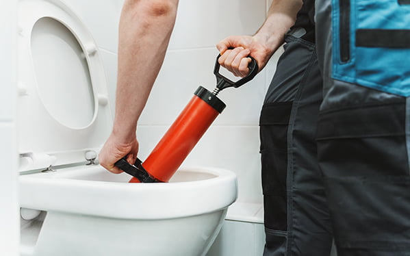 Professional drainage engineer using a red plunger to unblock a toilet, emphasizing effective drainage solutions for residential properties in Fulham.
