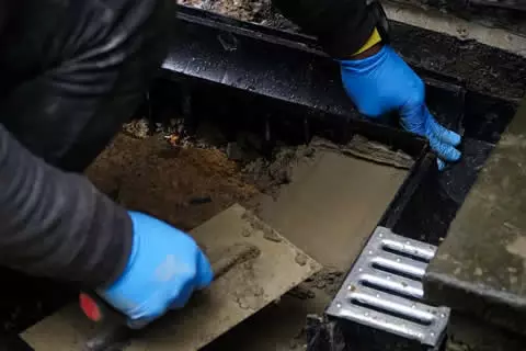 Worker in blue gloves performing gutter cleaning and maintenance, removing debris from drainage system, showcasing professional drain services for stadiums and event spaces.