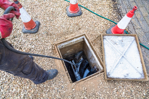 Professional conducting drain maintenance, using equipment to inspect drainage system, surrounded by safety cones, highlighting essential drain repair services in London.