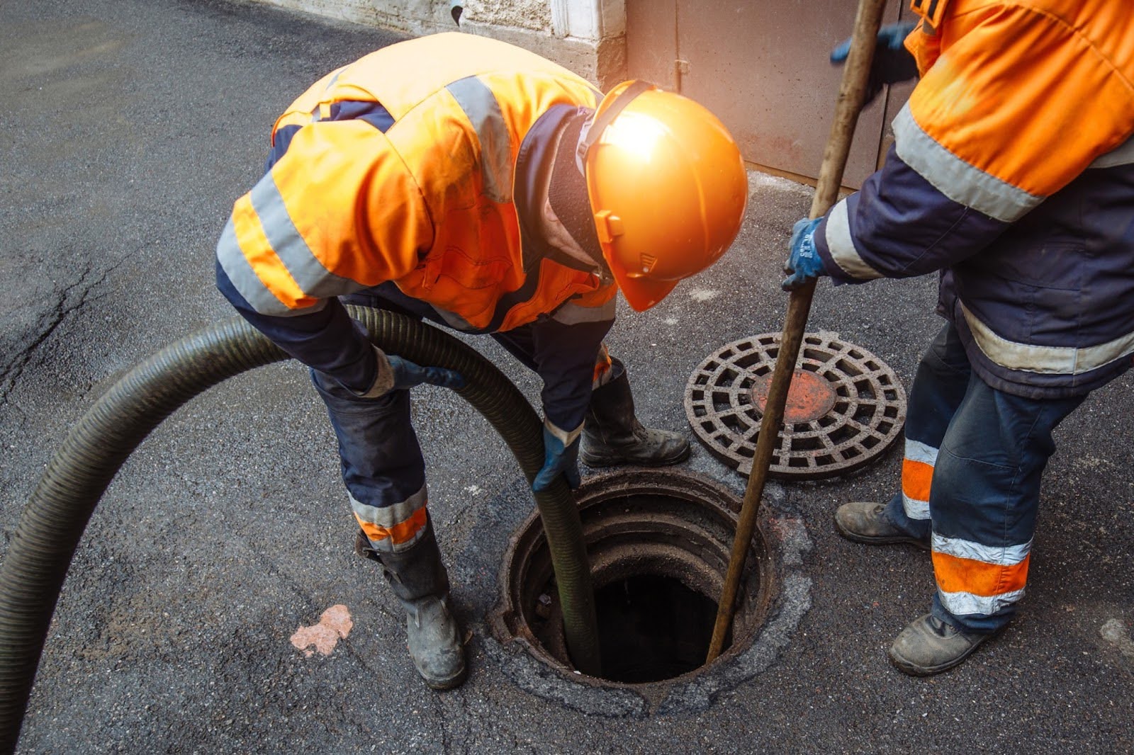 Workers in safety gear performing sewer cleaning with a vacuum hose and pole over a manhole in London, highlighting professional drainage services.